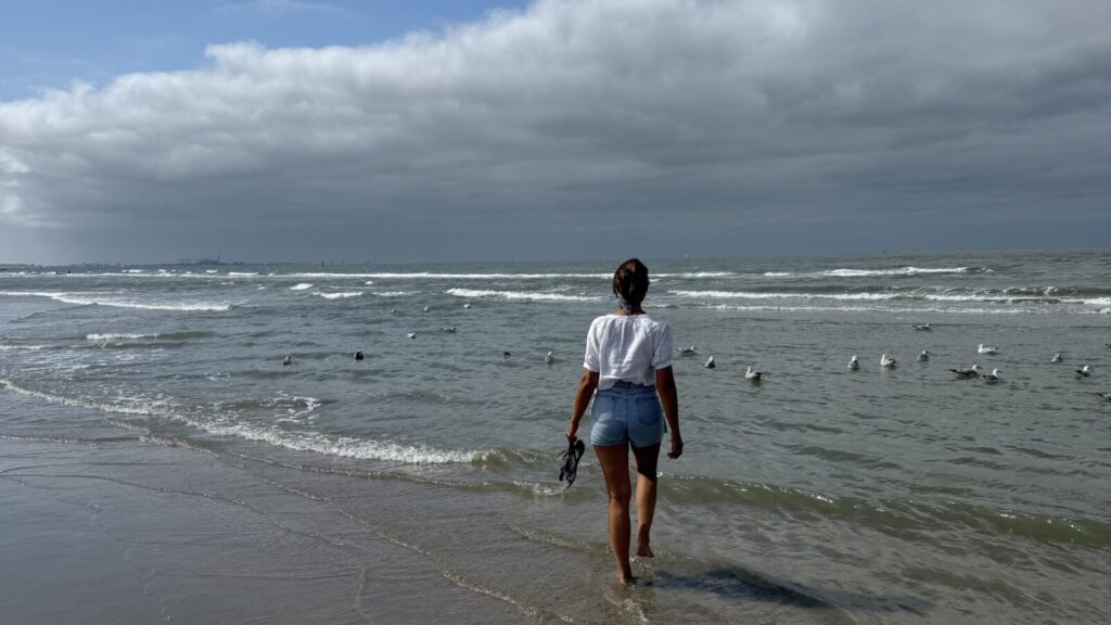 Vrouw loopt de zee in onder een bewolkte lucht - brain fog symptomen en je hoofd leegmaken